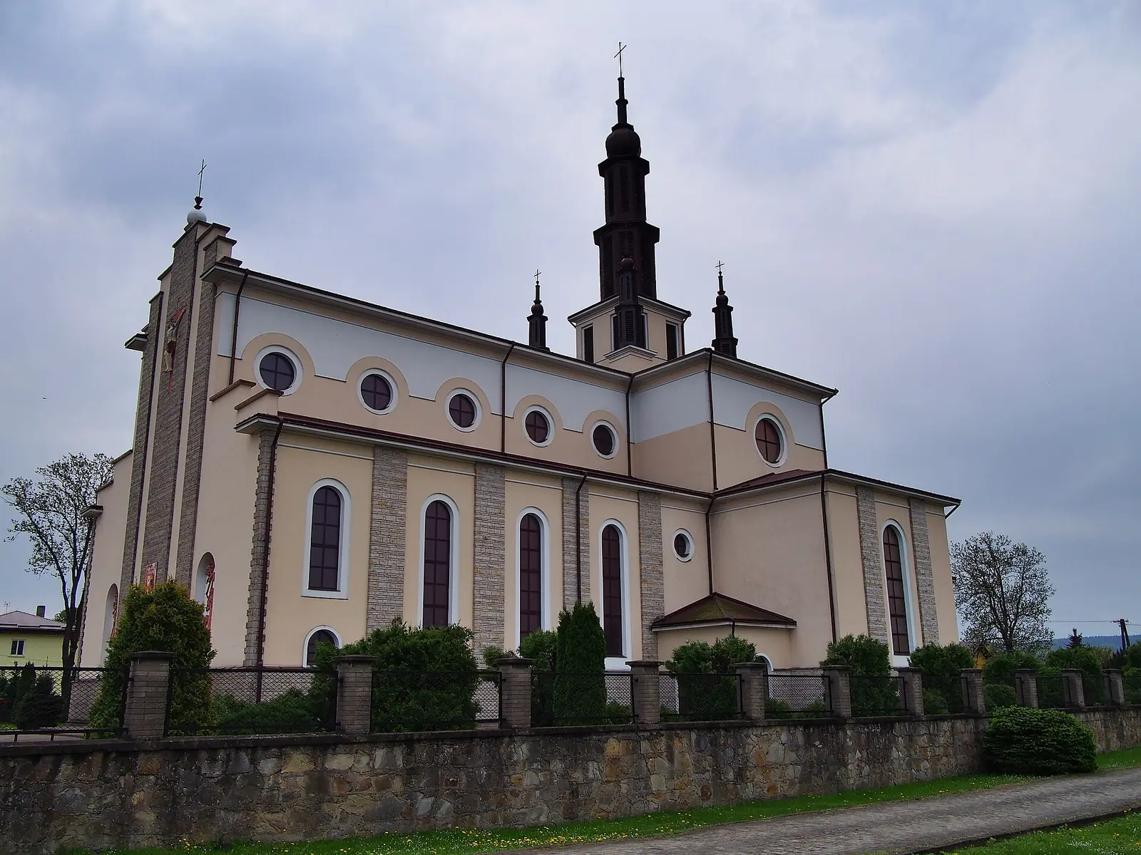 Kościół w Dubiecku za kamiennym murem i ogrodzeniem, pochmurne niebo