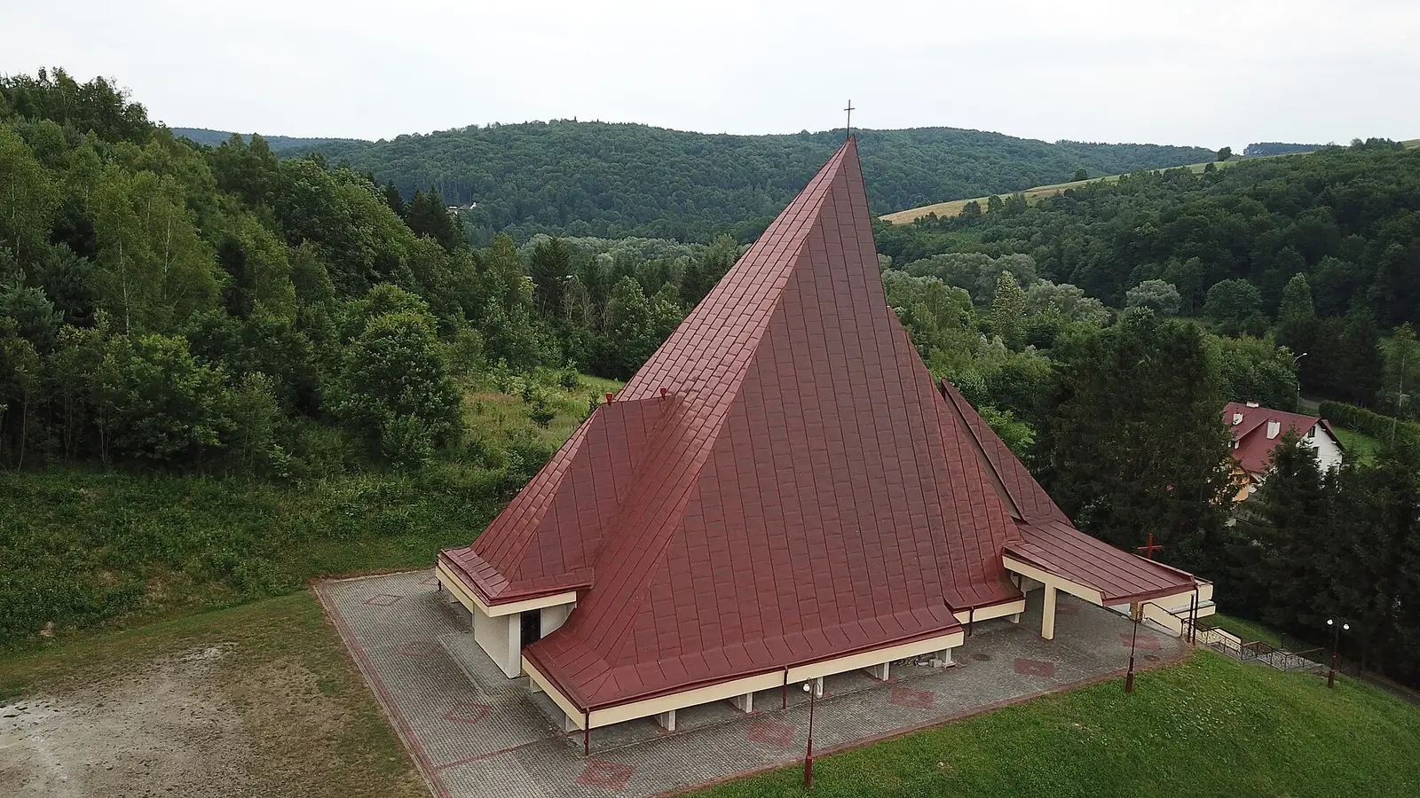 Kościół w Słonnem z lotu ptaka: strzelisty dach z czerwonej blachy wśród zalesionych wzgórz